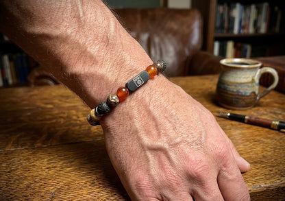 Мъжка гривна от естествени камъни – карнеол, вулканичен камък, тъмен слънчев камък и яспис, ръчно изработена от House of Astrology. Енергиен артефакт за сила, действие и вътрешен контрол.