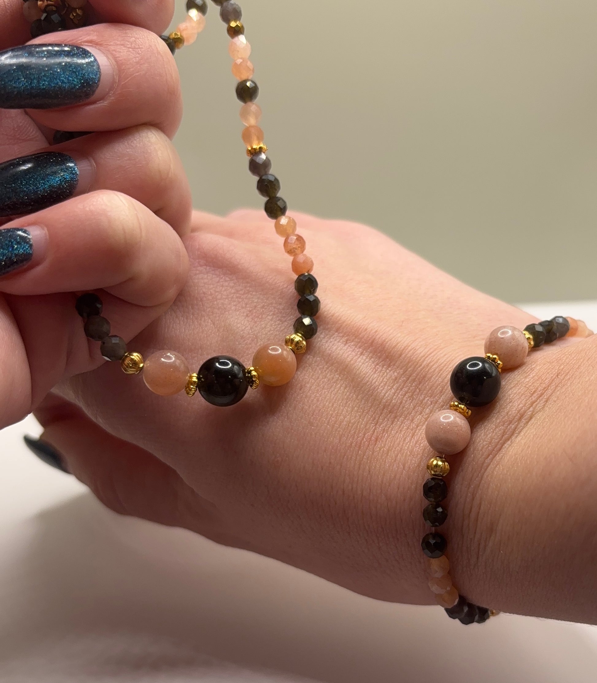 Ръчно изработена гривна от естествен слънчев камък и обсидиан с фасетирани мъниста и златни метални елементи, елегантно бижу с топъл блясък и дълбок черен контраст