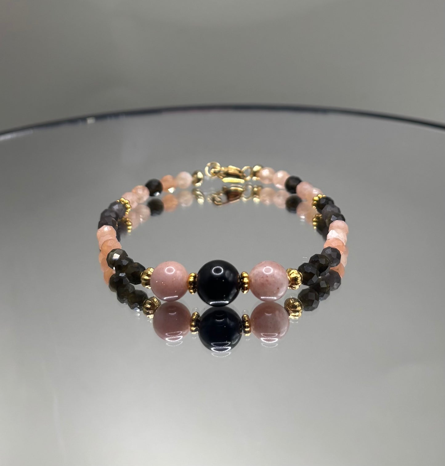 Ръчно изработена гривна от естествен слънчев камък и обсидиан с фасетирани мъниста и златни метални елементи, елегантно бижу с топъл блясък и дълбок черен контраст